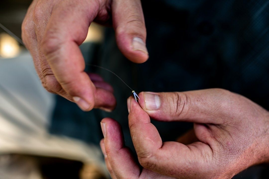 Hands tying a small fishing hook onto thin monofilament line
